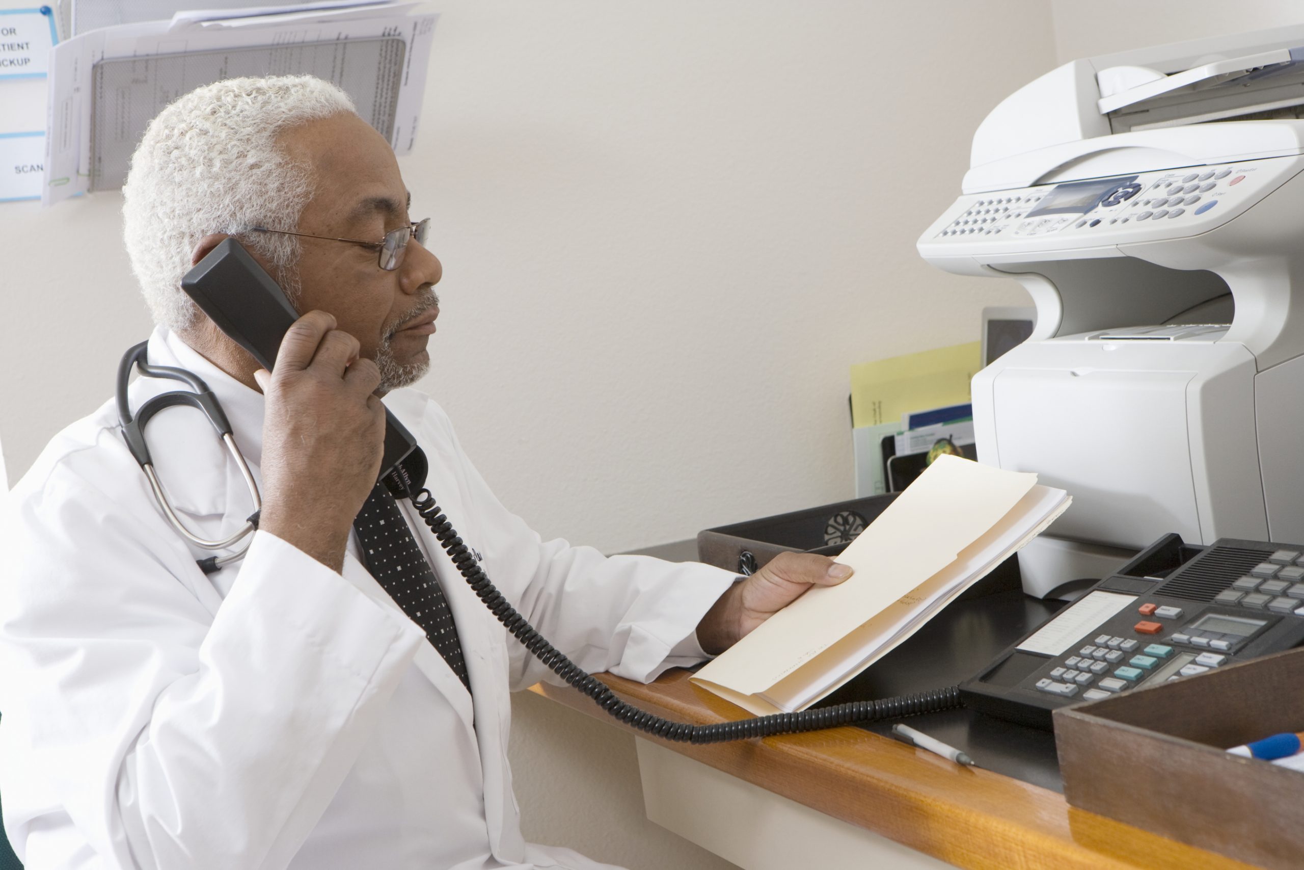 African American senior male doctor holding document while using phone